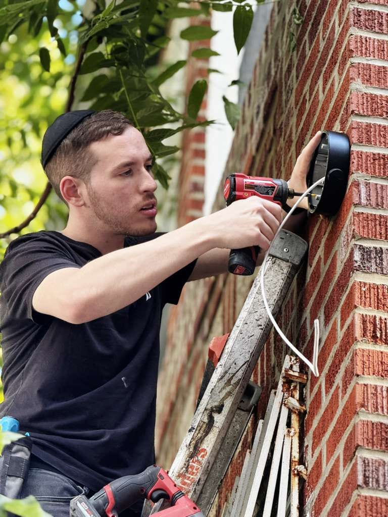 Sruly personally installing a camera housing on a brick wall, from the HD Installs build.