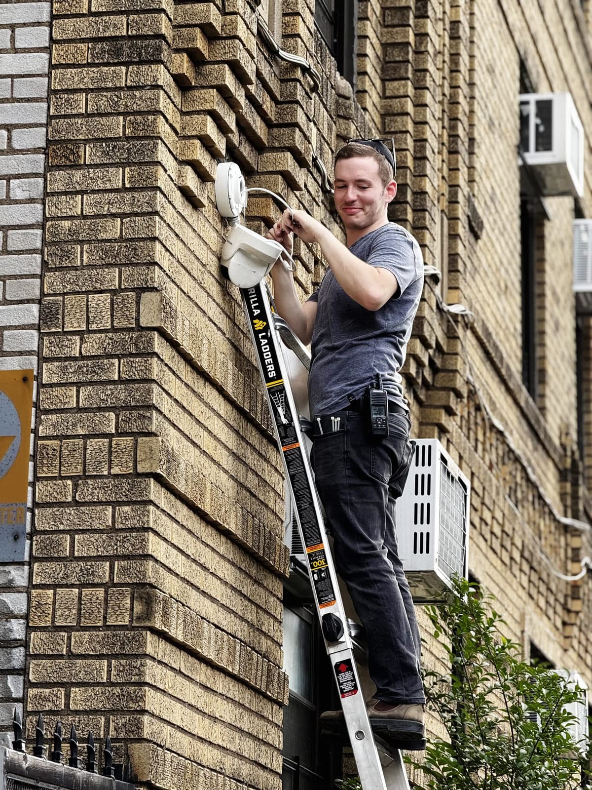 Sruly, the HD Installs owner-operator, on a ladder mid-install in daylight, smiling toward the camera.